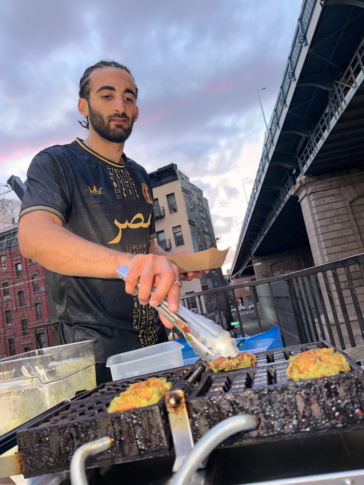 Mush cooking Fawaffles on a waffle iron at an NYC pop-up under the bridge at sunset