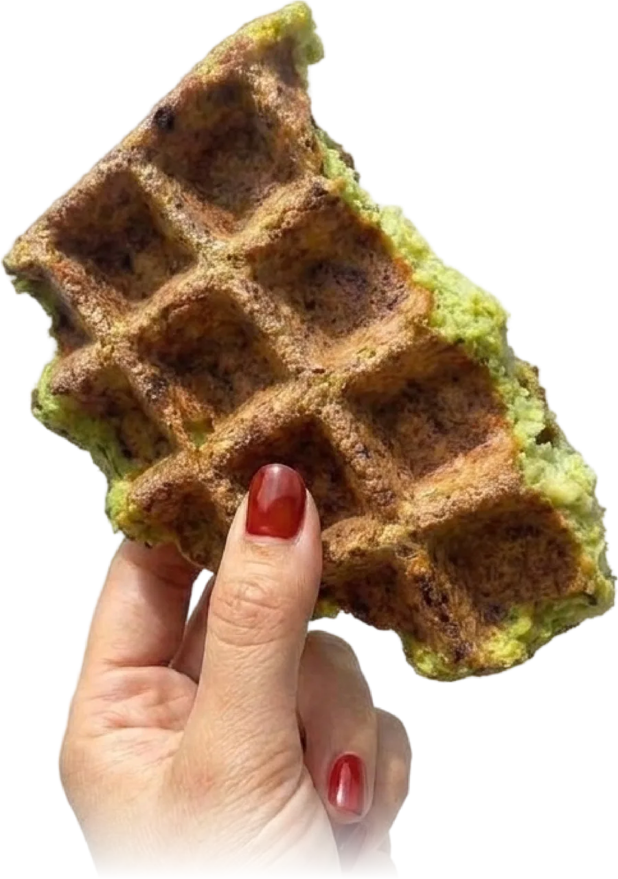 A hand holding up a crispy, herb-green Fawaffle with a bite taken out